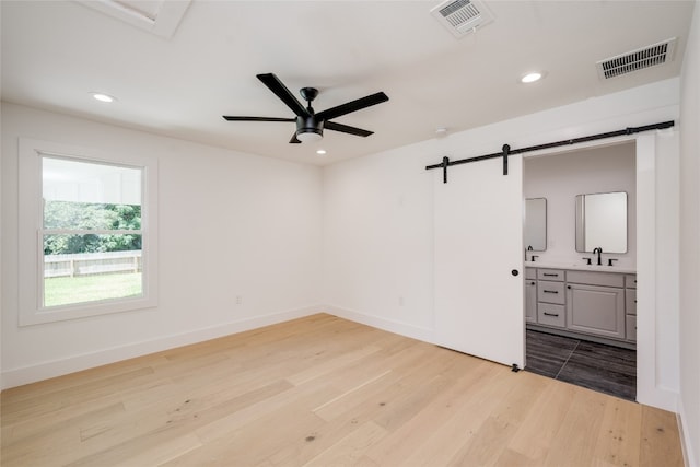 unfurnished bedroom featuring ceiling fan, connected bathroom, light hardwood / wood-style flooring, and a barn door