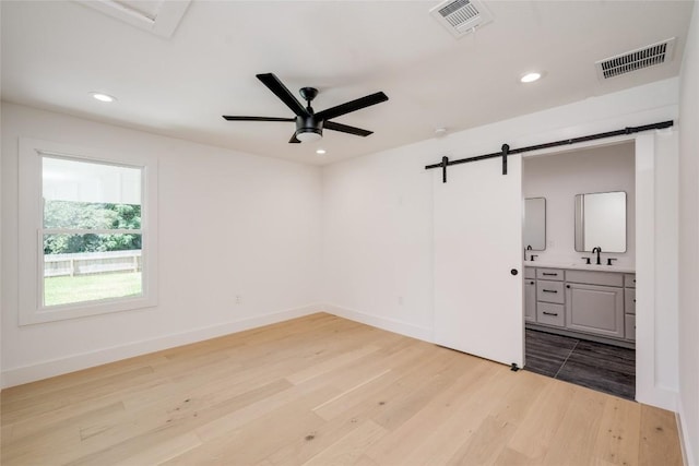 empty room featuring light wood finished floors, a barn door, visible vents, and recessed lighting