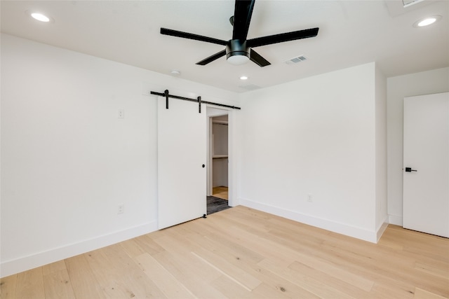 unfurnished bedroom featuring ceiling fan, light hardwood / wood-style floors, and a barn door