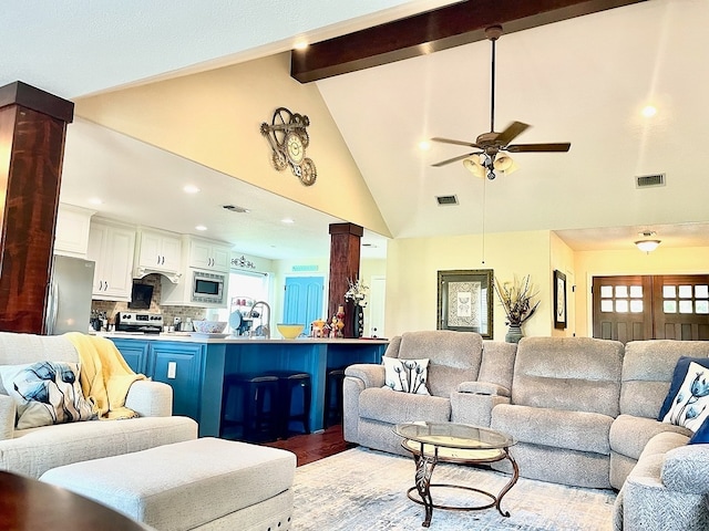 living room featuring ceiling fan, light hardwood / wood-style flooring, plenty of natural light, decorative columns, and beamed ceiling