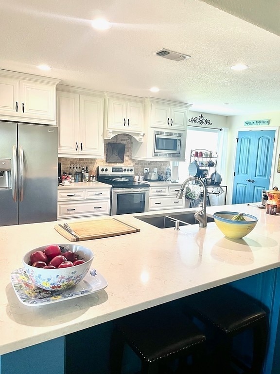 kitchen featuring appliances with stainless steel finishes, premium range hood, tasteful backsplash, sink, and white cabinets