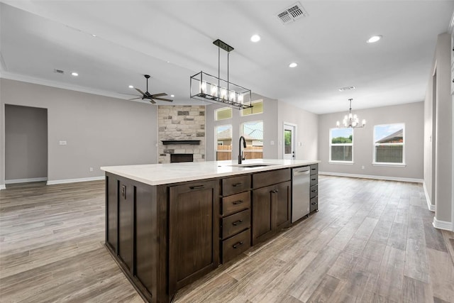 kitchen featuring a center island with sink, open floor plan, light countertops, a stone fireplace, and a sink