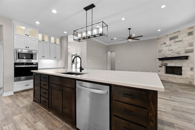 kitchen featuring appliances with stainless steel finishes, light hardwood / wood-style floors, a fireplace, white cabinets, and ceiling fan with notable chandelier