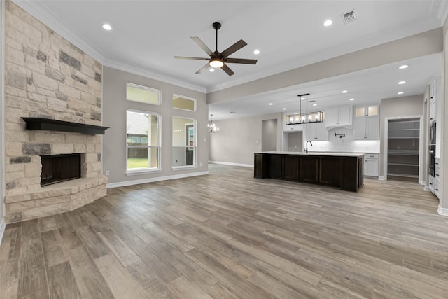 kitchen featuring light wood-type flooring, decorative light fixtures, ornamental molding, and an island with sink