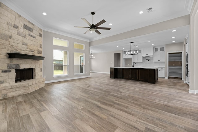 unfurnished living room with light wood-type flooring, ceiling fan with notable chandelier, a stone fireplace, and ornamental molding