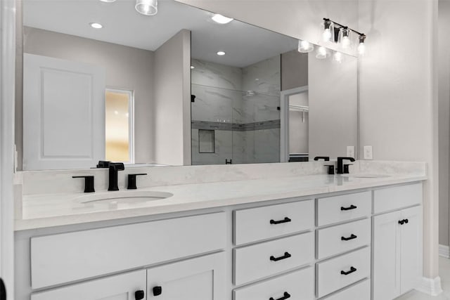 full bath featuring double vanity, a marble finish shower, a sink, and recessed lighting