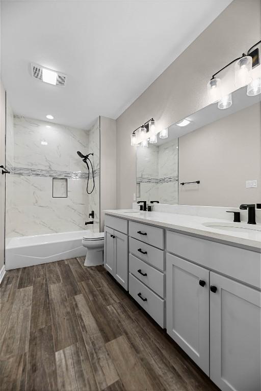 full bathroom featuring toilet, tiled shower / bath combo, dual bowl vanity, and wood-type flooring