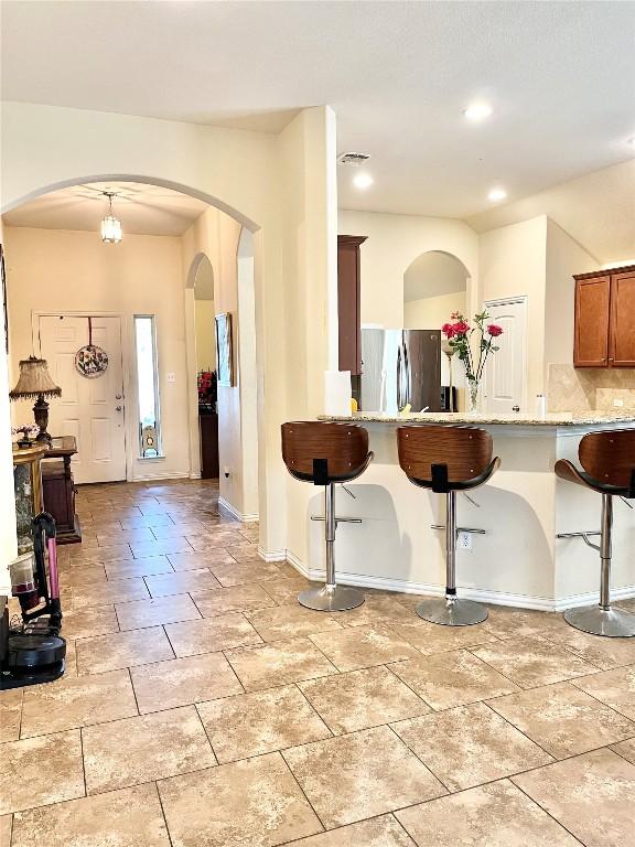 interior space featuring pendant lighting, stainless steel refrigerator, backsplash, light tile patterned floors, and light stone countertops