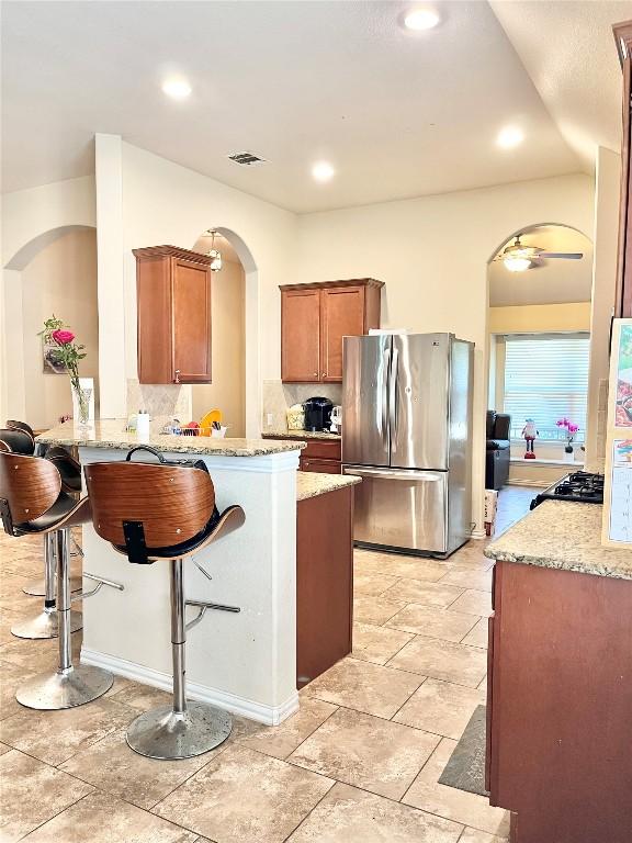 kitchen with light tile patterned floors, a kitchen bar, kitchen peninsula, stainless steel refrigerator, and decorative backsplash