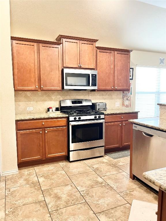 kitchen featuring light tile patterned flooring, backsplash, stainless steel appliances, and light stone countertops