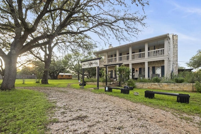 back of house with a lawn, stone siding, and a balcony