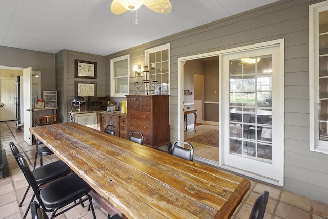tiled dining room featuring a ceiling fan and wood walls