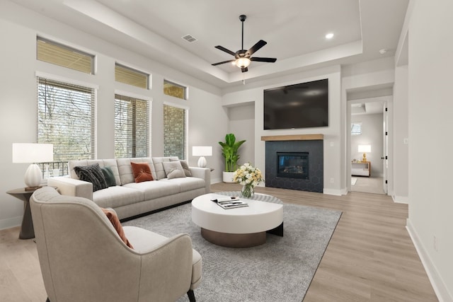 living room featuring baseboards, a tray ceiling, a glass covered fireplace, and light wood-style floors