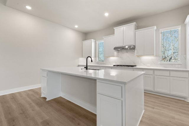 kitchen featuring light countertops, an island with sink, a sink, and white cabinets