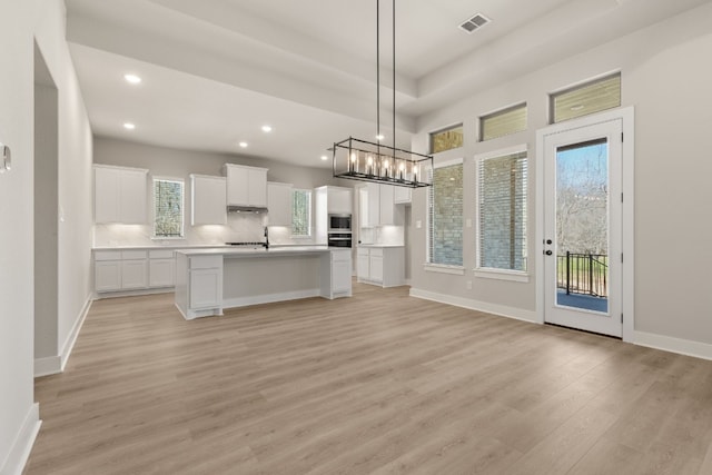 kitchen with white cabinetry, black oven, light countertops, stainless steel microwave, and a center island with sink