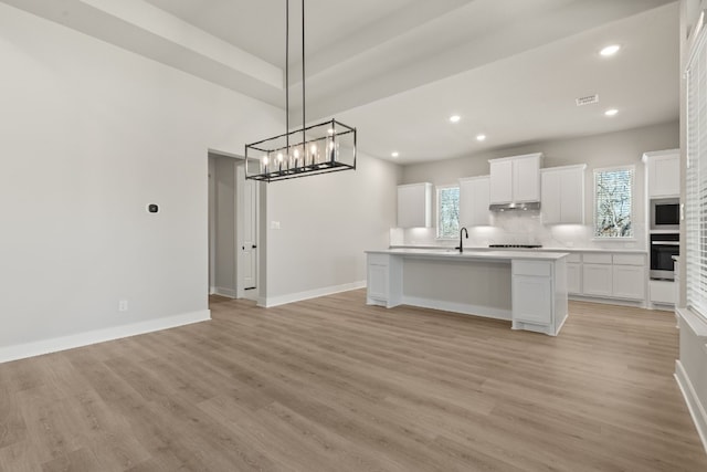 kitchen featuring wall oven, a center island with sink, white cabinets, decorative light fixtures, and light countertops