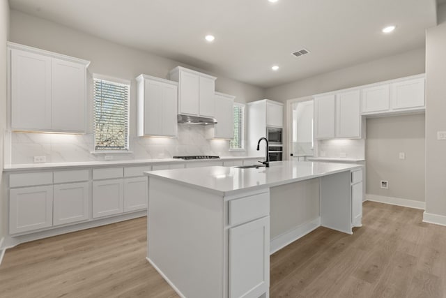 kitchen featuring an island with sink, white cabinets, and light countertops