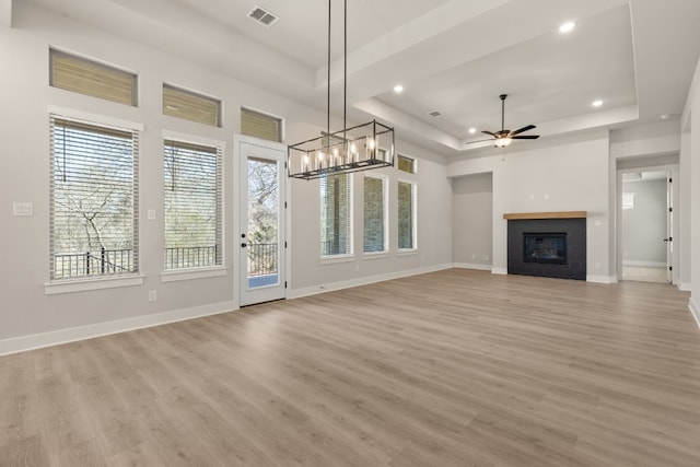 unfurnished living room with baseboards, visible vents, a ceiling fan, a glass covered fireplace, and a tray ceiling