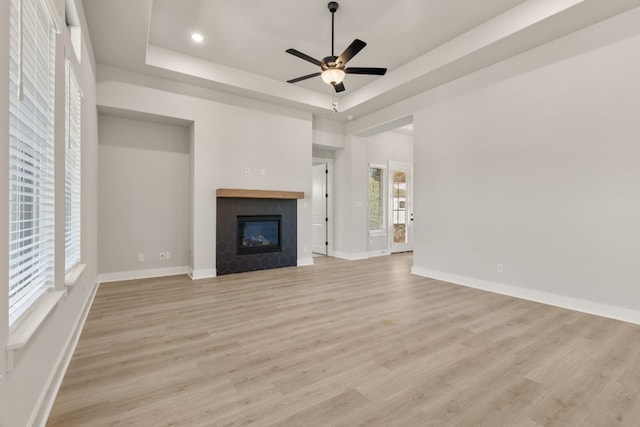 unfurnished living room with light wood-style floors, baseboards, a tray ceiling, and a tiled fireplace