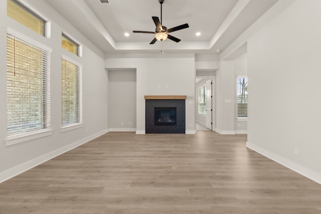 unfurnished living room with baseboards, a raised ceiling, a glass covered fireplace, light wood-type flooring, and recessed lighting