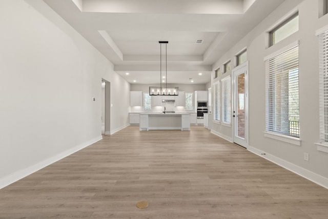 unfurnished living room featuring a raised ceiling, baseboards, visible vents, and light wood finished floors