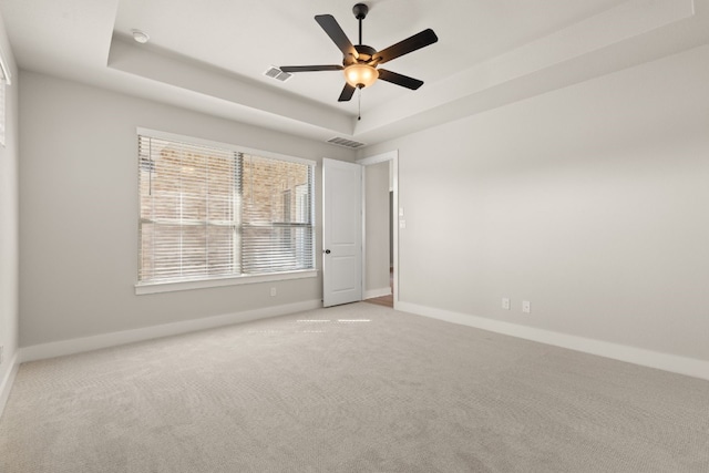 carpeted empty room featuring a ceiling fan, visible vents, a tray ceiling, and baseboards