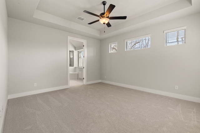 spare room with a wealth of natural light, a tray ceiling, visible vents, and baseboards