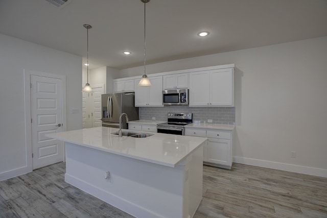 kitchen with appliances with stainless steel finishes, decorative light fixtures, white cabinetry, and a kitchen island with sink