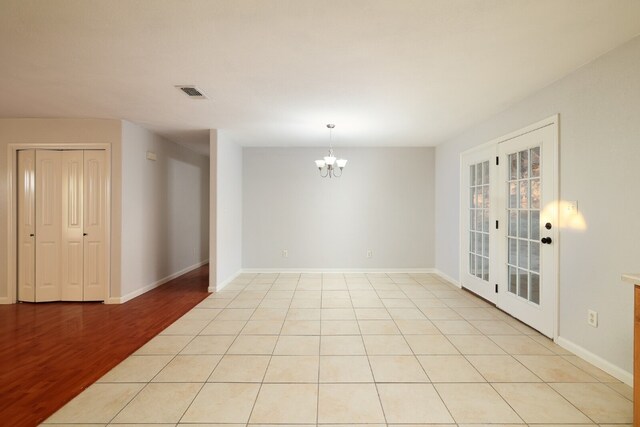 empty room with light hardwood / wood-style flooring, a chandelier, and french doors