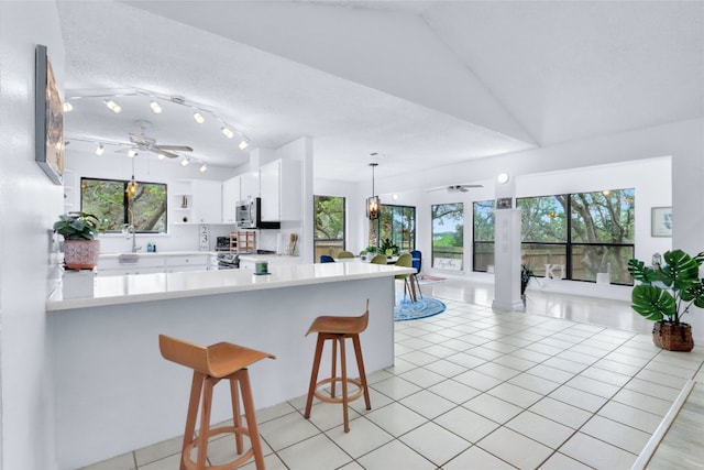 kitchen featuring a breakfast bar, stainless steel appliances, ceiling fan, kitchen peninsula, and white cabinets