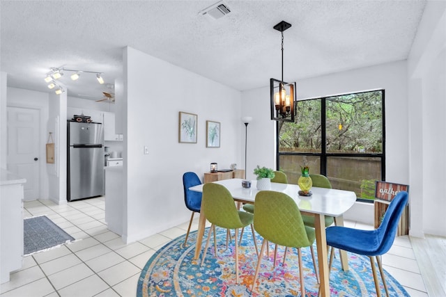 tiled dining space with rail lighting, a textured ceiling, and a chandelier