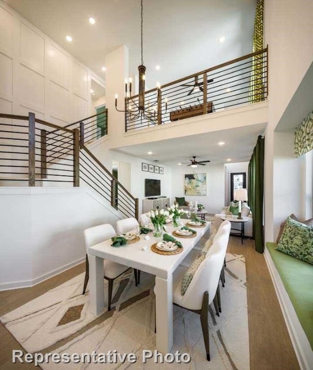 dining room featuring ceiling fan with notable chandelier, a towering ceiling, and light hardwood / wood-style flooring