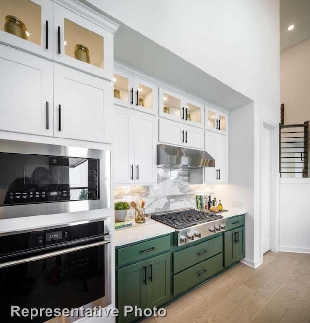 kitchen with appliances with stainless steel finishes, decorative backsplash, light hardwood / wood-style floors, white cabinets, and green cabinets