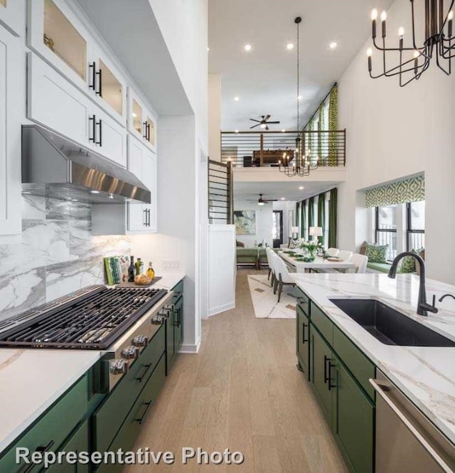 kitchen with white cabinets, ceiling fan with notable chandelier, stainless steel appliances, light wood-type flooring, and sink