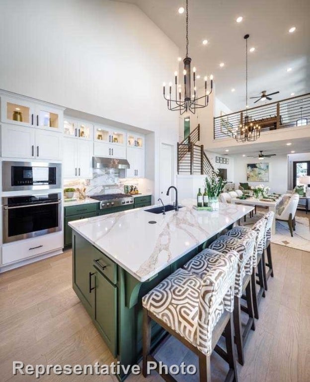 kitchen with pendant lighting, ceiling fan with notable chandelier, white cabinetry, high vaulted ceiling, and stainless steel appliances