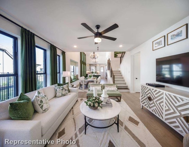 living room featuring ceiling fan with notable chandelier and light hardwood / wood-style flooring