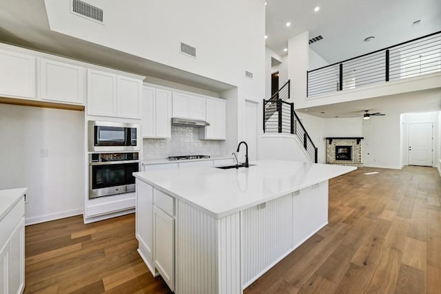 kitchen with built in microwave, oven, an island with sink, and white cabinets