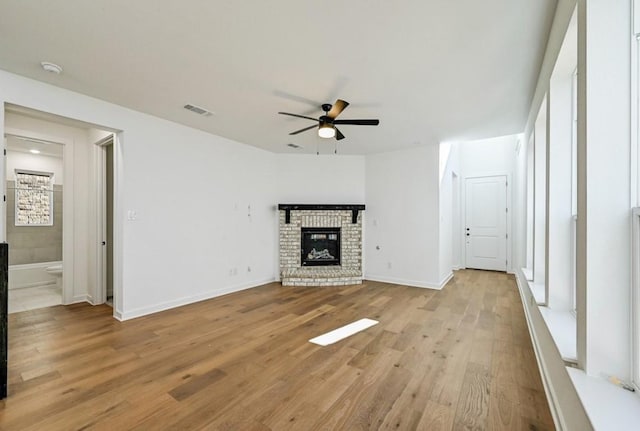 unfurnished living room featuring ceiling fan, a brick fireplace, and light hardwood / wood-style floors