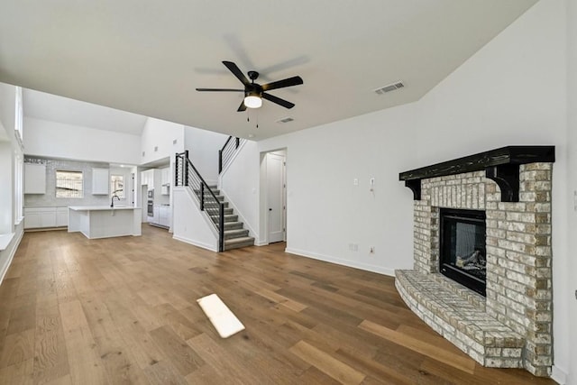 unfurnished living room with ceiling fan, a fireplace, sink, and light hardwood / wood-style flooring