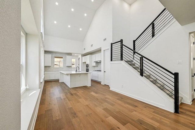 kitchen featuring sink, white cabinetry, light wood-type flooring, an island with sink, and a towering ceiling