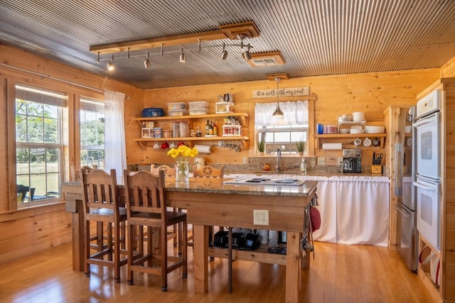 bar featuring pendant lighting, white appliances, light wood-style floors, and wooden walls