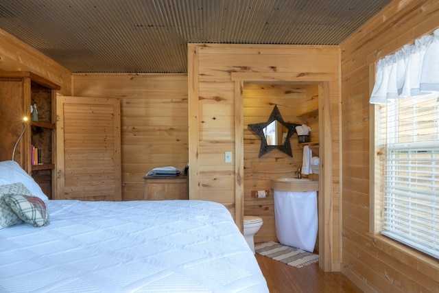 bedroom featuring wood walls, hardwood / wood-style floors, and ensuite bathroom