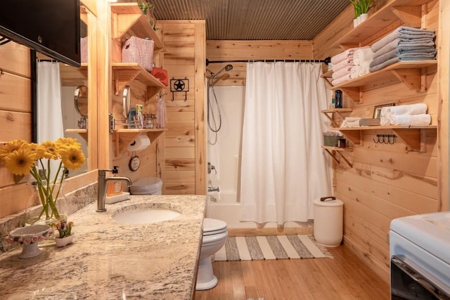 bathroom featuring shower / tub combo, wooden walls, toilet, wood finished floors, and vanity