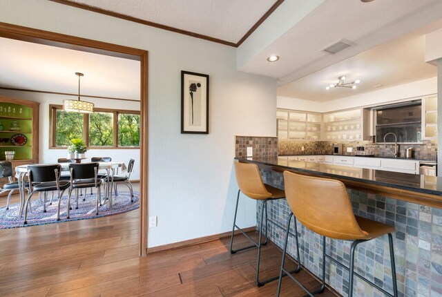 kitchen featuring hardwood / wood-style floors, baseboards, ornamental molding, dark countertops, and tasteful backsplash