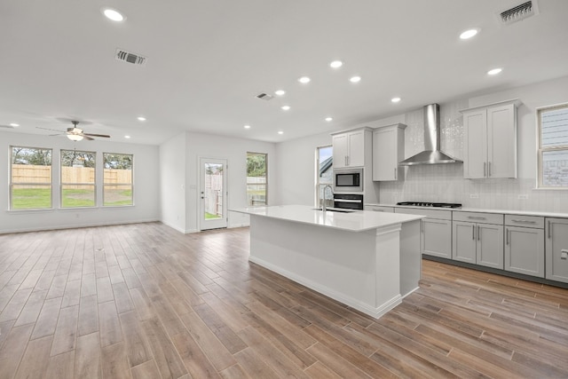 kitchen with appliances with stainless steel finishes, visible vents, wall chimney range hood, and gray cabinetry