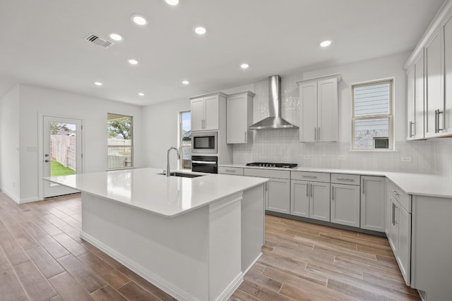 kitchen featuring wall chimney exhaust hood, sink, light hardwood / wood-style floors, black oven, and stainless steel microwave