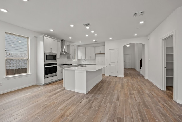 kitchen with arched walkways, stainless steel appliances, visible vents, a sink, and wall chimney exhaust hood