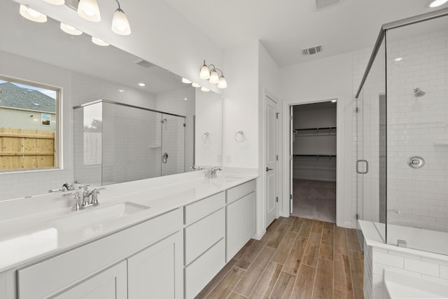 bathroom with a walk in closet, wood finish floors, visible vents, a stall shower, and a sink