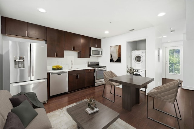 kitchen with stacked washer / drying machine, backsplash, sink, appliances with stainless steel finishes, and dark wood-type flooring