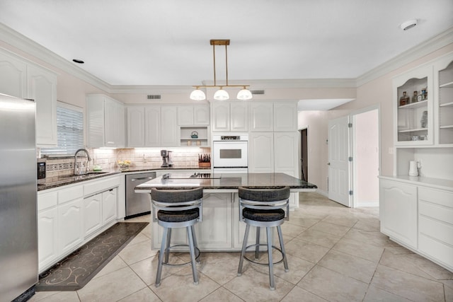 kitchen with stainless steel appliances, white cabinets, sink, a kitchen island, and dark stone countertops